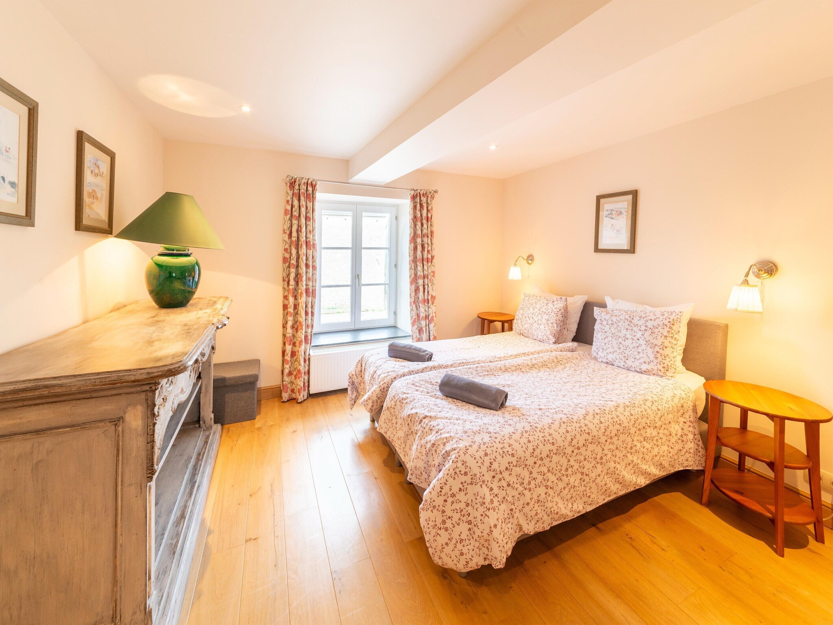 Une chambre avec deux lits, une fenêtre avec des rideaux, une lampe et une petite table.