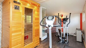 Una sauna con paredes de madera y puerta de vidrio, una bicicleta estática y una cinta de correr en una habitación con pared estampada y pared de piedra.