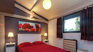 Un dormitorio con una cama, dos mesitas de noche con lámparas, un radiador, una ventana con cortinas y un cuadro en la pared.