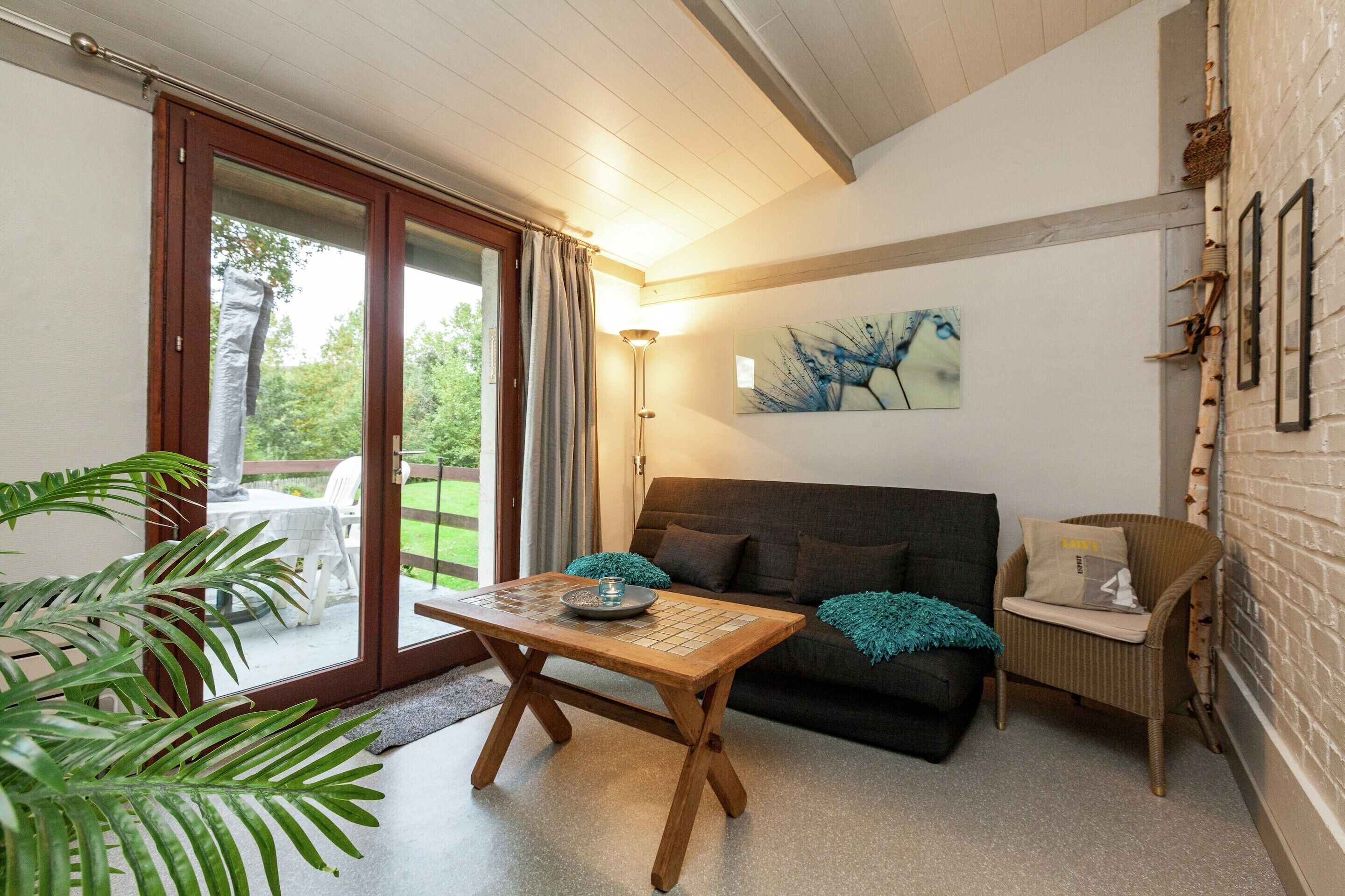 A cozy living room with a sofa, a wooden coffee table, and a dining table. There is a sliding glass door leading to an outdoor area with a table and chairs.