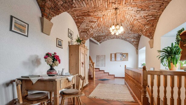 Ein rustikales Interieur mit einem Holzespeisetisch, Stühlen, einer Treppe und einer Ziegeldecke.