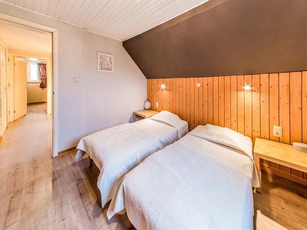 A room with two beds, wooden walls, a wooden ceiling, a small bedside table with a lamp, and a picture on the wall.