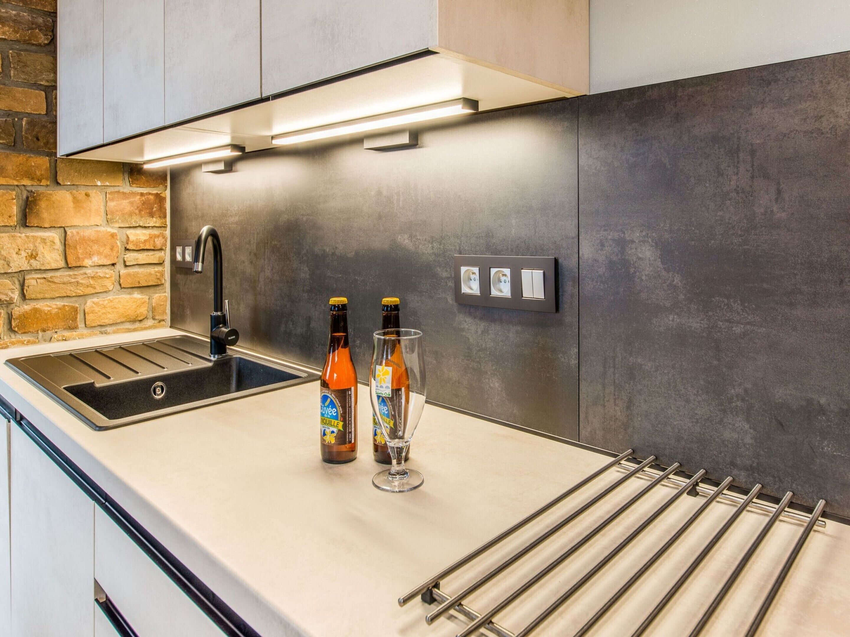 A modern kitchen with a built-in sink, a stainless steel faucet, and a wine glass. There are two bottles of beer on the counter.
