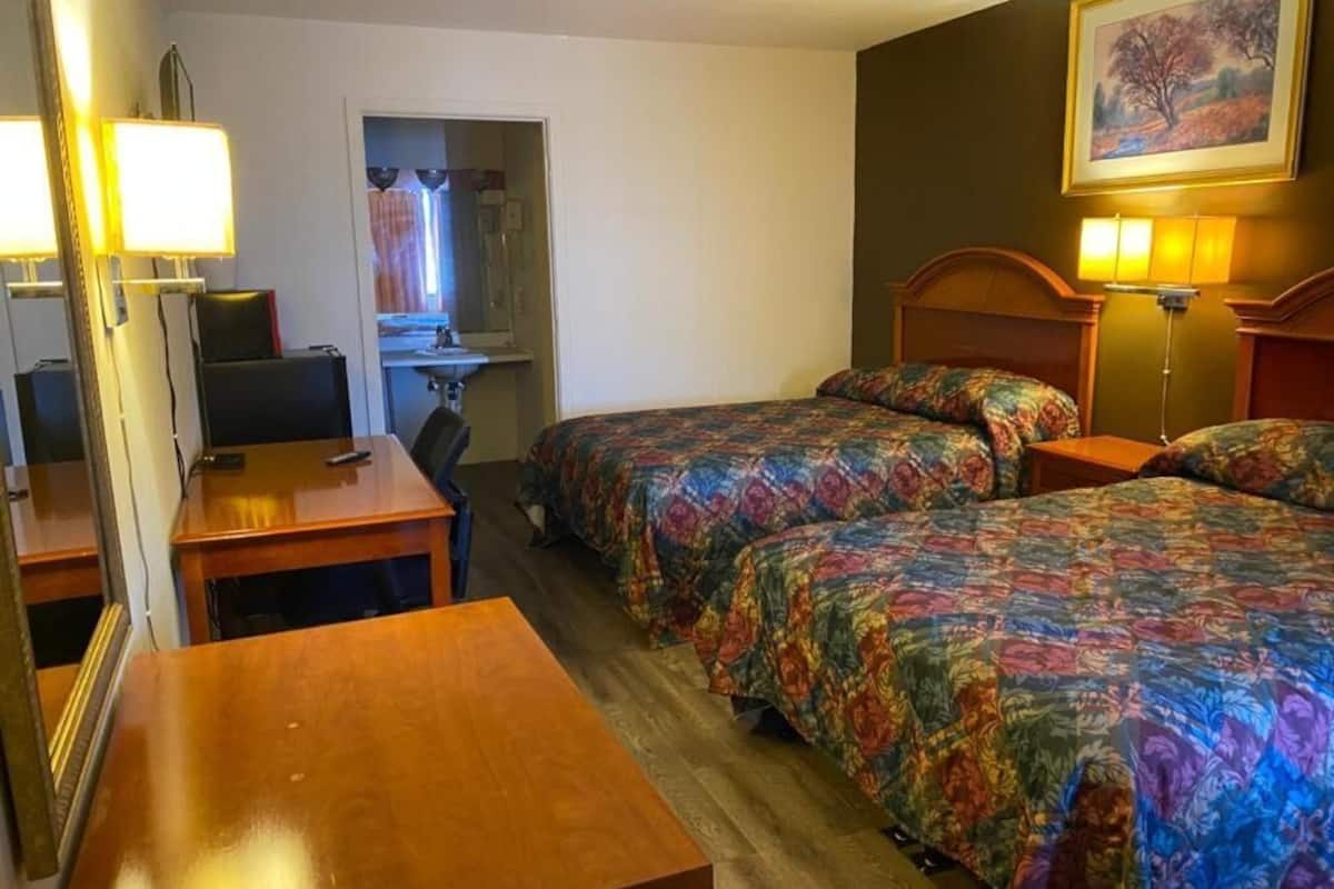 A hotel room with two beds, a desk, a chair, and a mirror.