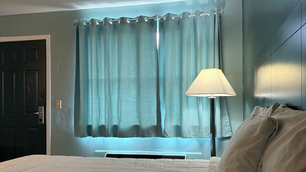 A bedroom with a bed, a window with curtains, a lamp, and a door.
