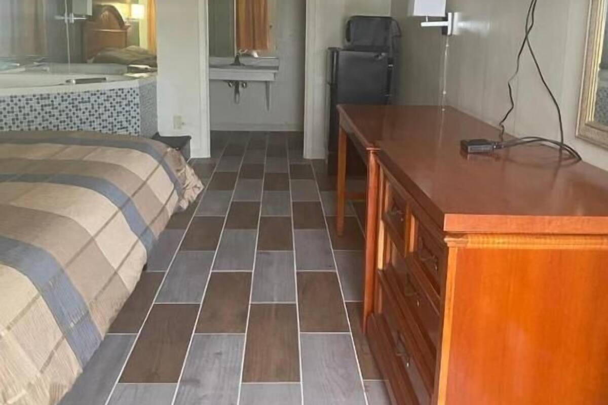 A hotel room with a bed, a wooden dresser, a television, and a bathroom with a mirror and sink.