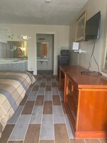 Habitación de hotel con cama, cómoda de madera, televisor y baño con espejo y lavamanos.