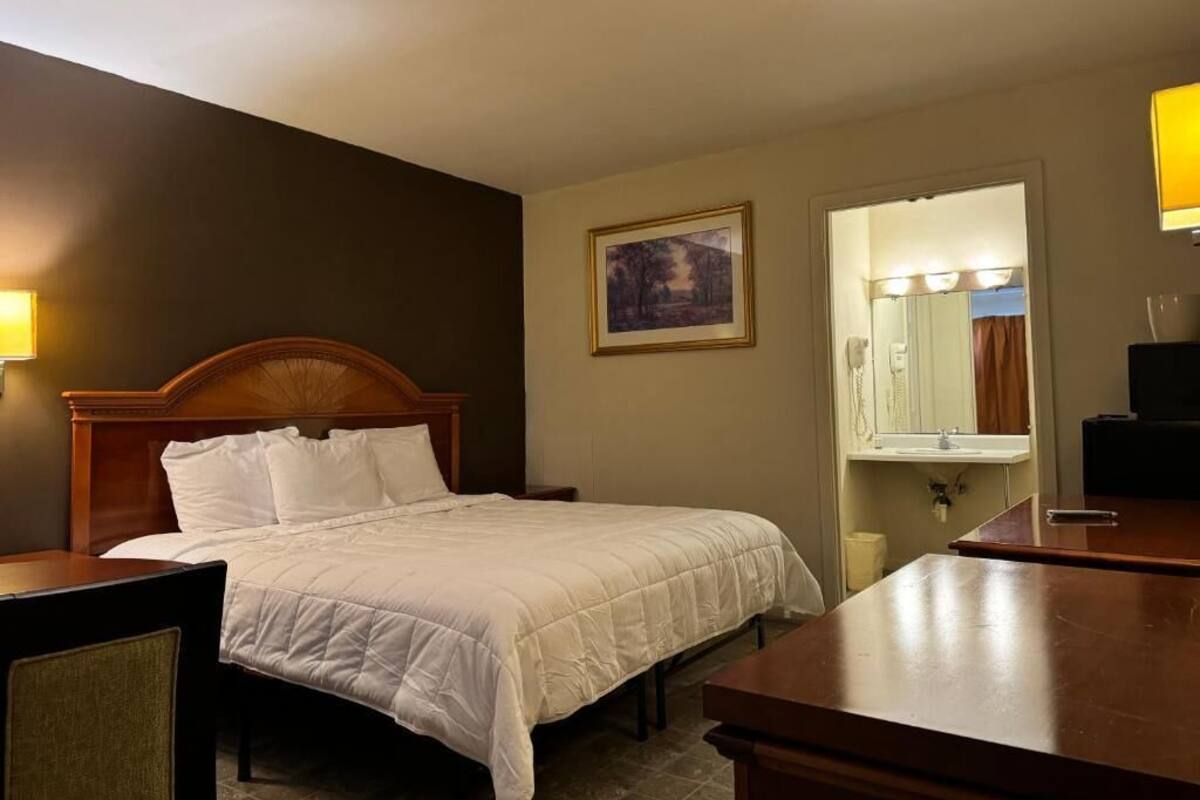 A hotel room with a bed, bedside table, lamp, and a painting on the wall.