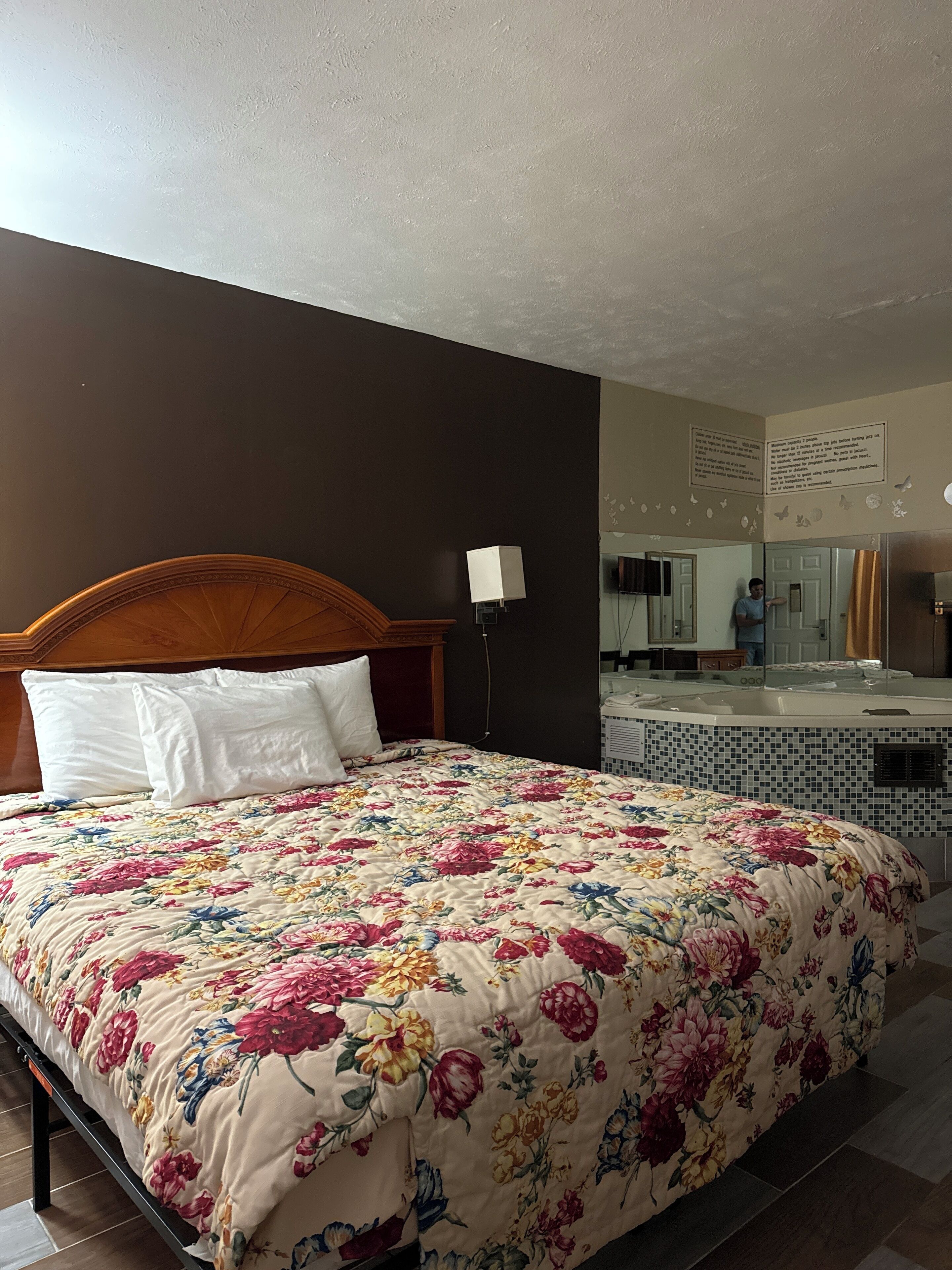 Una camera d'albergo con un letto, un comodino, una lampada, un bagno con una vasca e uno specchio.