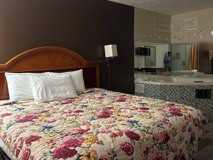 A hotel room with a bed, a nightstand, a lamp, a bathroom with a bathtub, and a mirror.