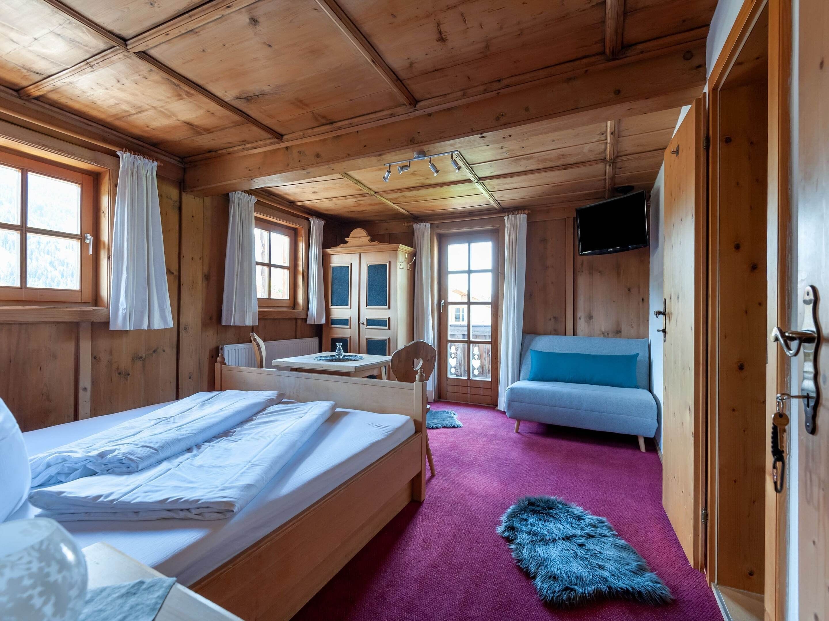 A wooden cabin room with a bed, a sofa, a table, and a television.