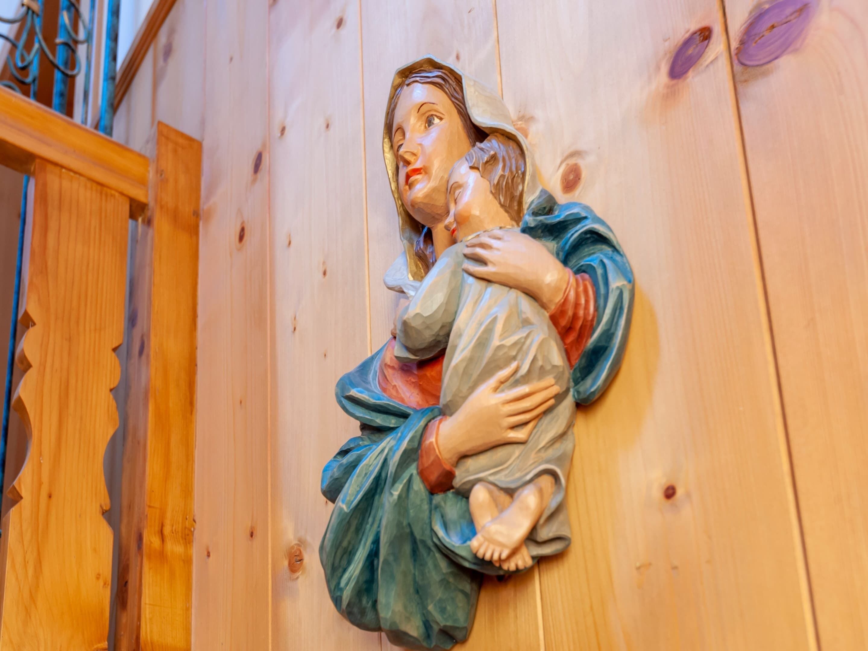 A wooden sculpture of a woman holding a child, likely a religious icon, mounted on a wooden wall.