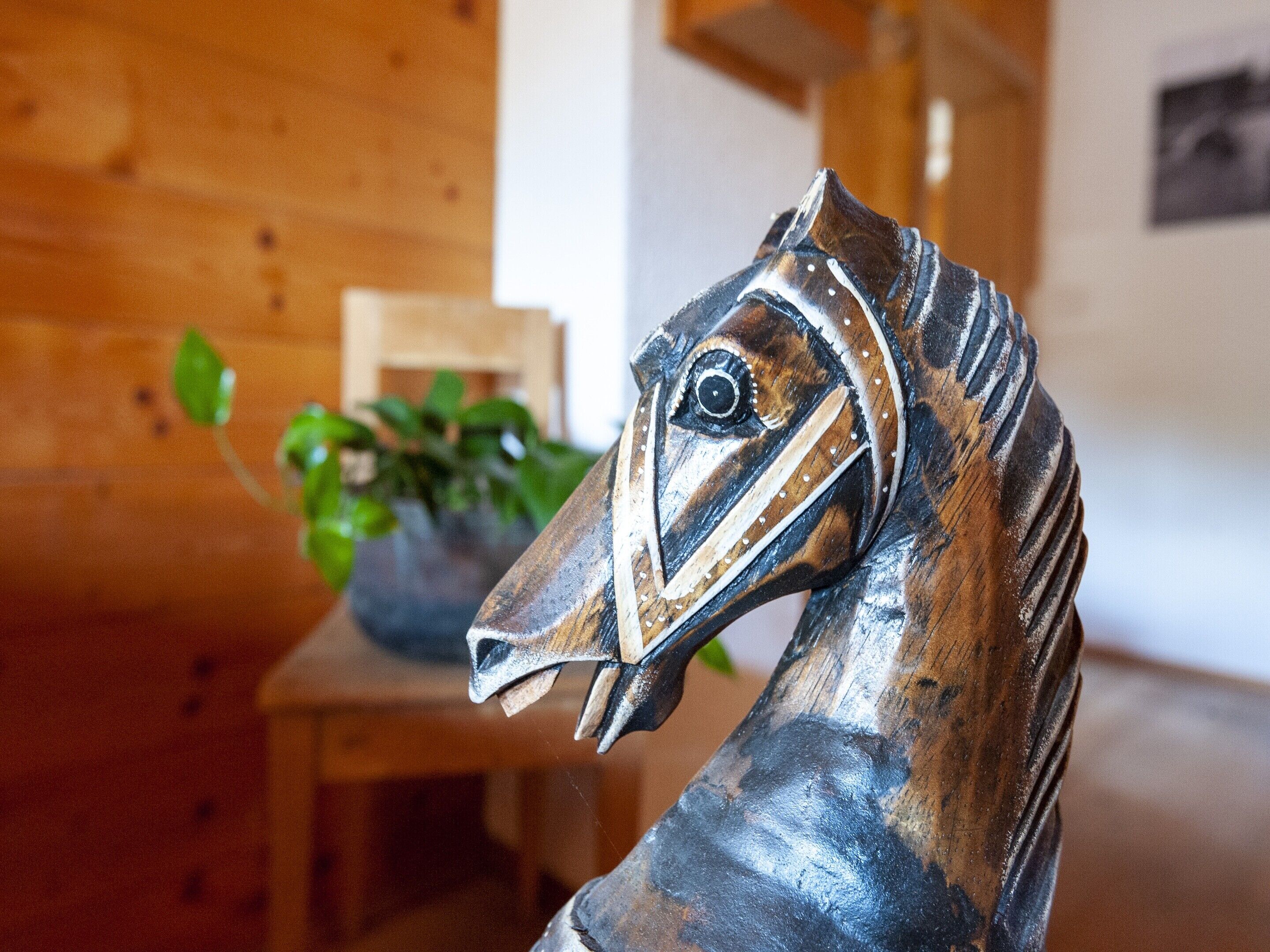 Ein Holzstuhl mit einer Metallskulptur eines Pferdes davor.