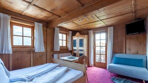 A wooden cabin with a bed, a small table, a chair, a sofa, and a TV mounted on the wall. - Beautiful Flat in Kirchberg Near the ski Area (Kirchberg in Tirol)