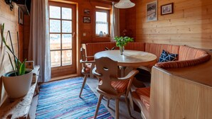 A cozy wooden cabin interior with a round dining table, cushioned seating, and a large window offering a view of the outdoors. - Beautiful Flat in Kirchberg Near the ski Area (Kirchberg in Tirol)