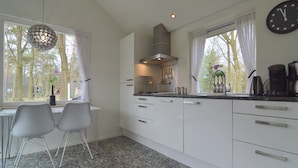 A modern kitchen with white cabinets, a dining area with two chairs, and a large window with curtains. - Holiday Home in Stramproy Near Nature Reserves (Stramproy)
