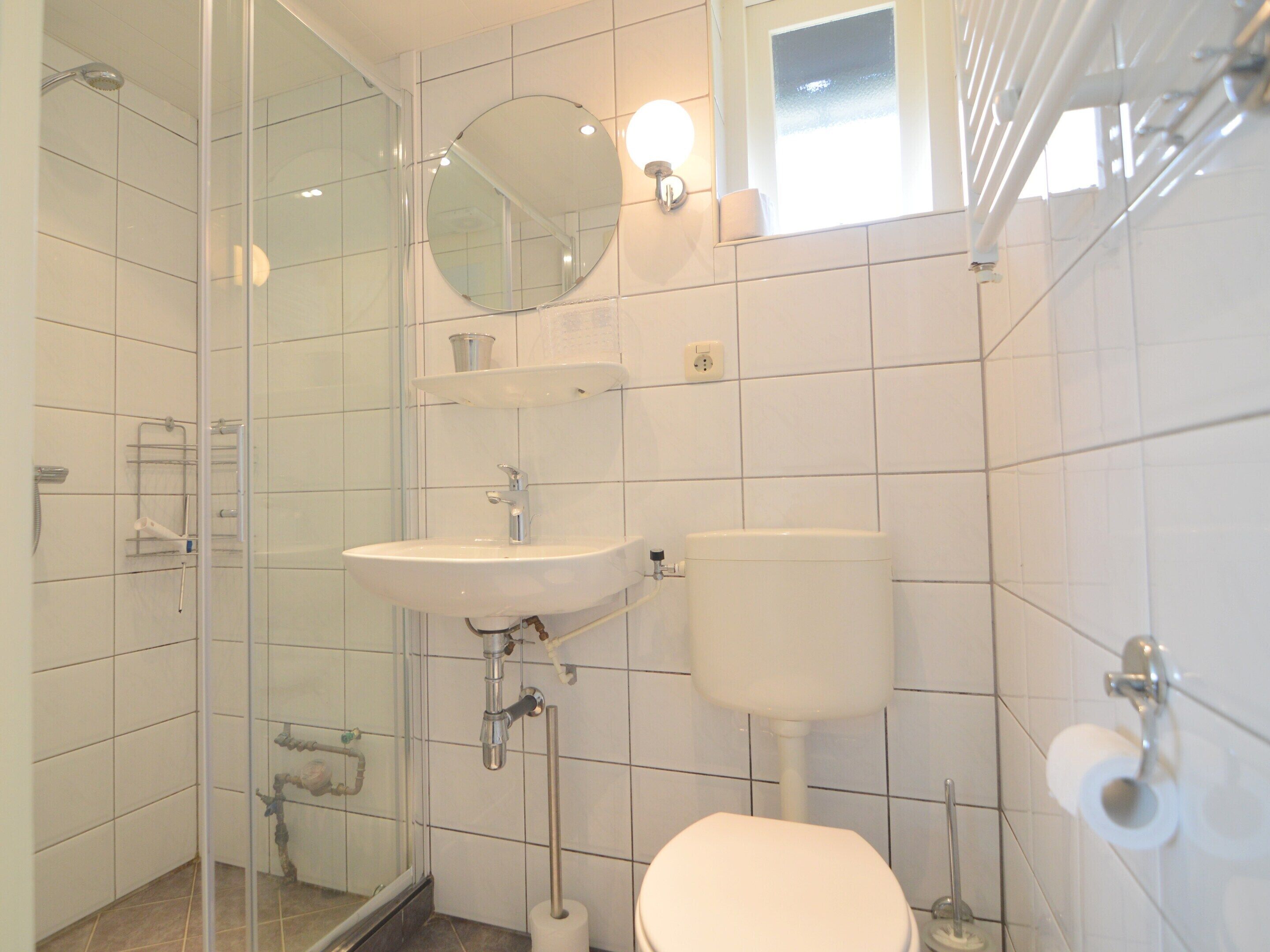 Ein Badezimmer mit Duschkabine aus Glas, einem Waschbecken inklusive Spiegel und einer Toilette.