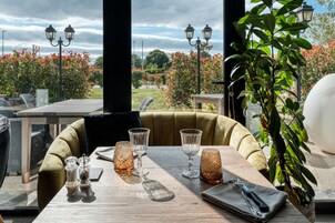 Una mesa de comedor con cristalería y un cuchillo, un banco acolchado y una planta en maceta.