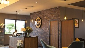 Un área de recepción con suelo de mármol, mostrador de madera, dos sillones tapizados y un espejo grande en la pared.