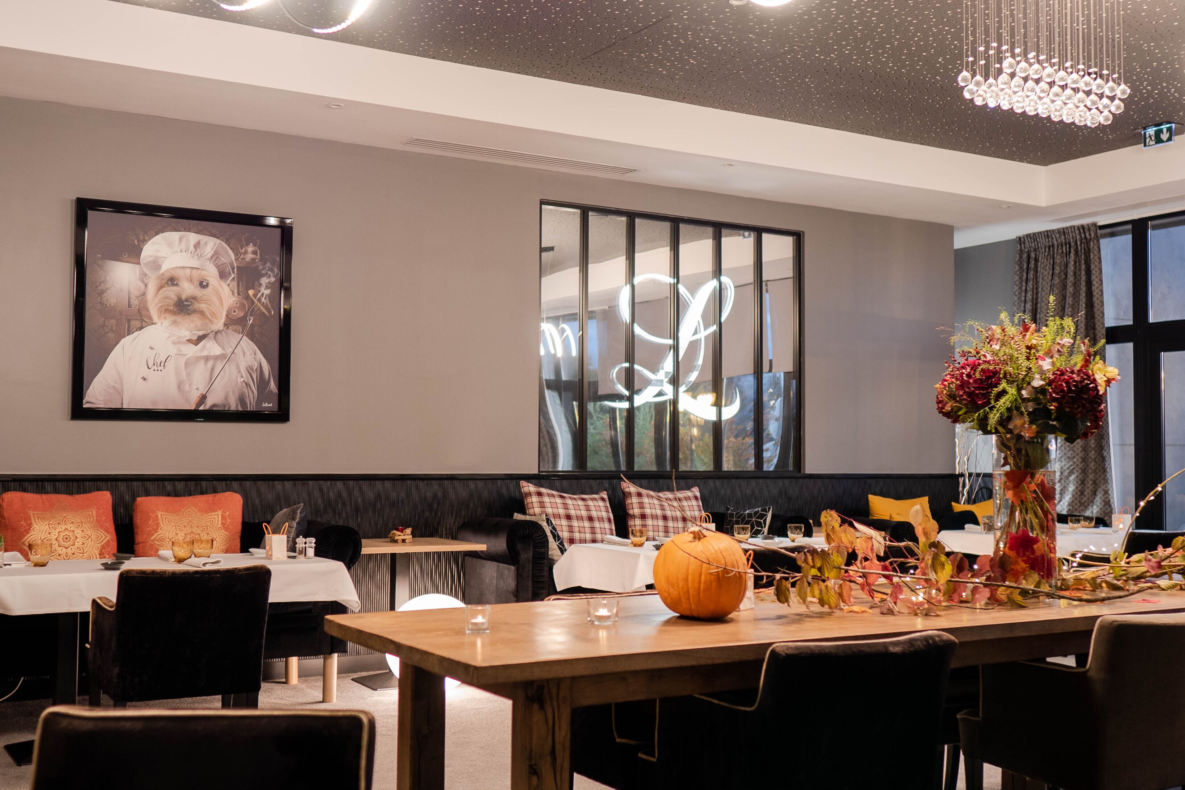 A dining area with tables set for guests, a large framed picture on the wall, and a decorative vase with flowers on the table.