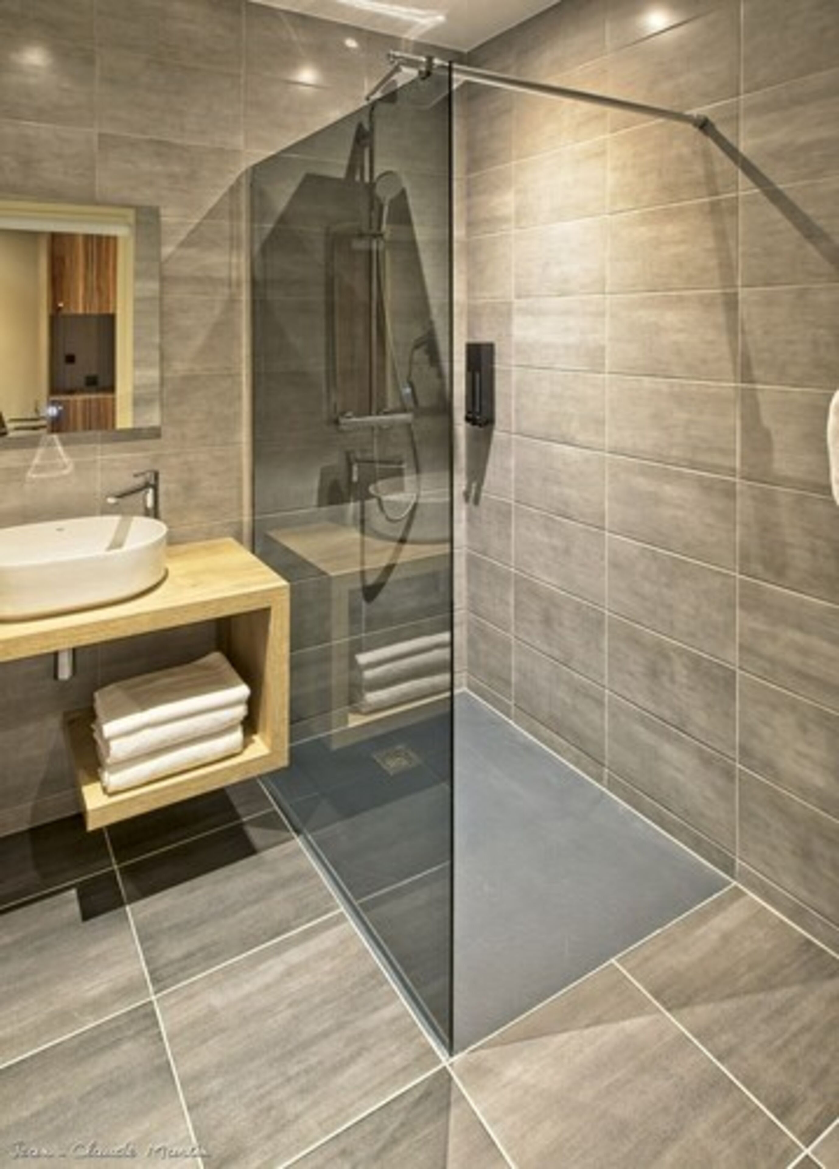 A modern bathroom with a glass-enclosed shower, a wooden vanity, and a large mirror.