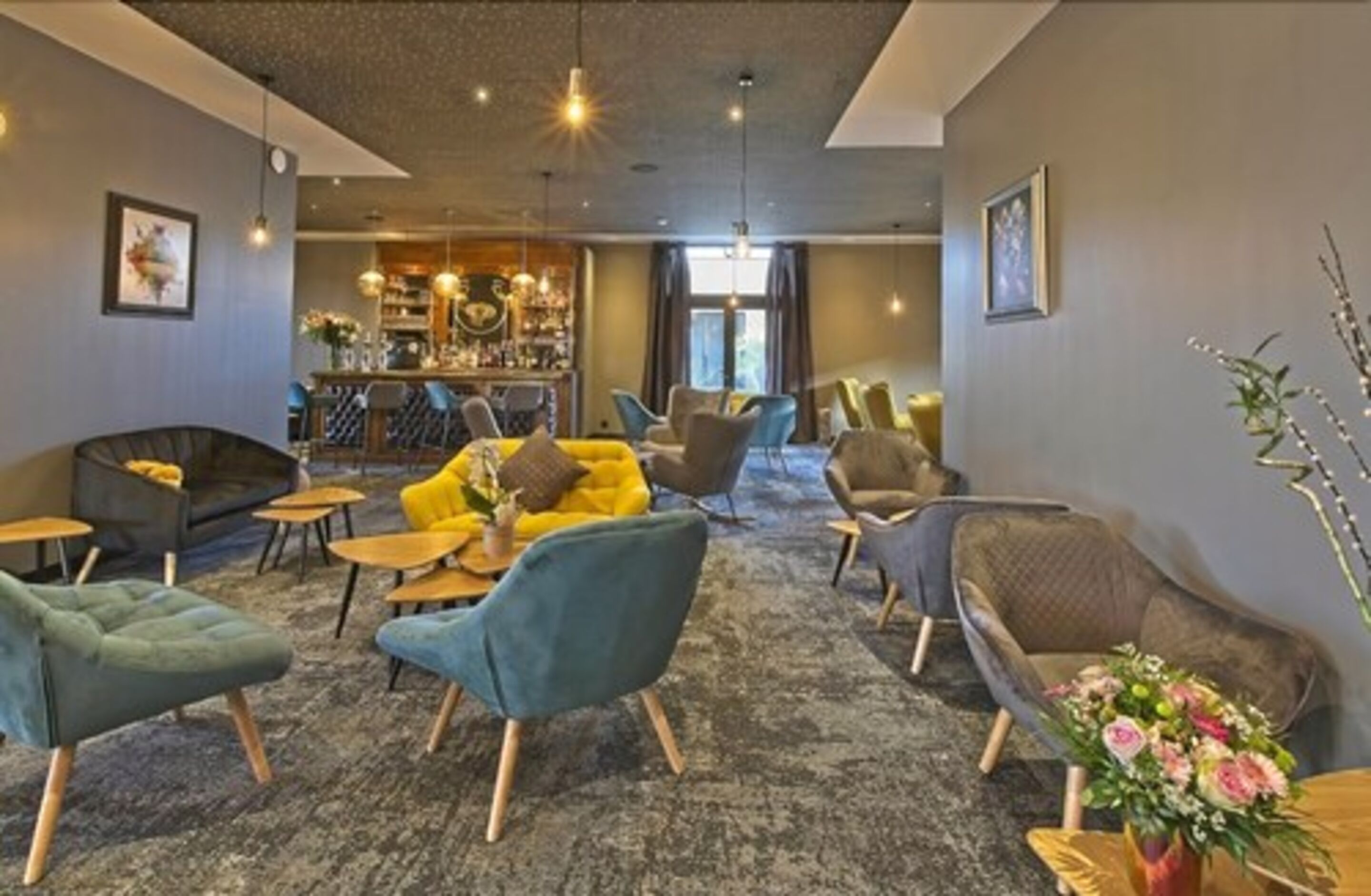 Un espace lounge moderne avec un bar en arrière-plan, doté de sièges confortables et d’une palette de couleurs neutres.