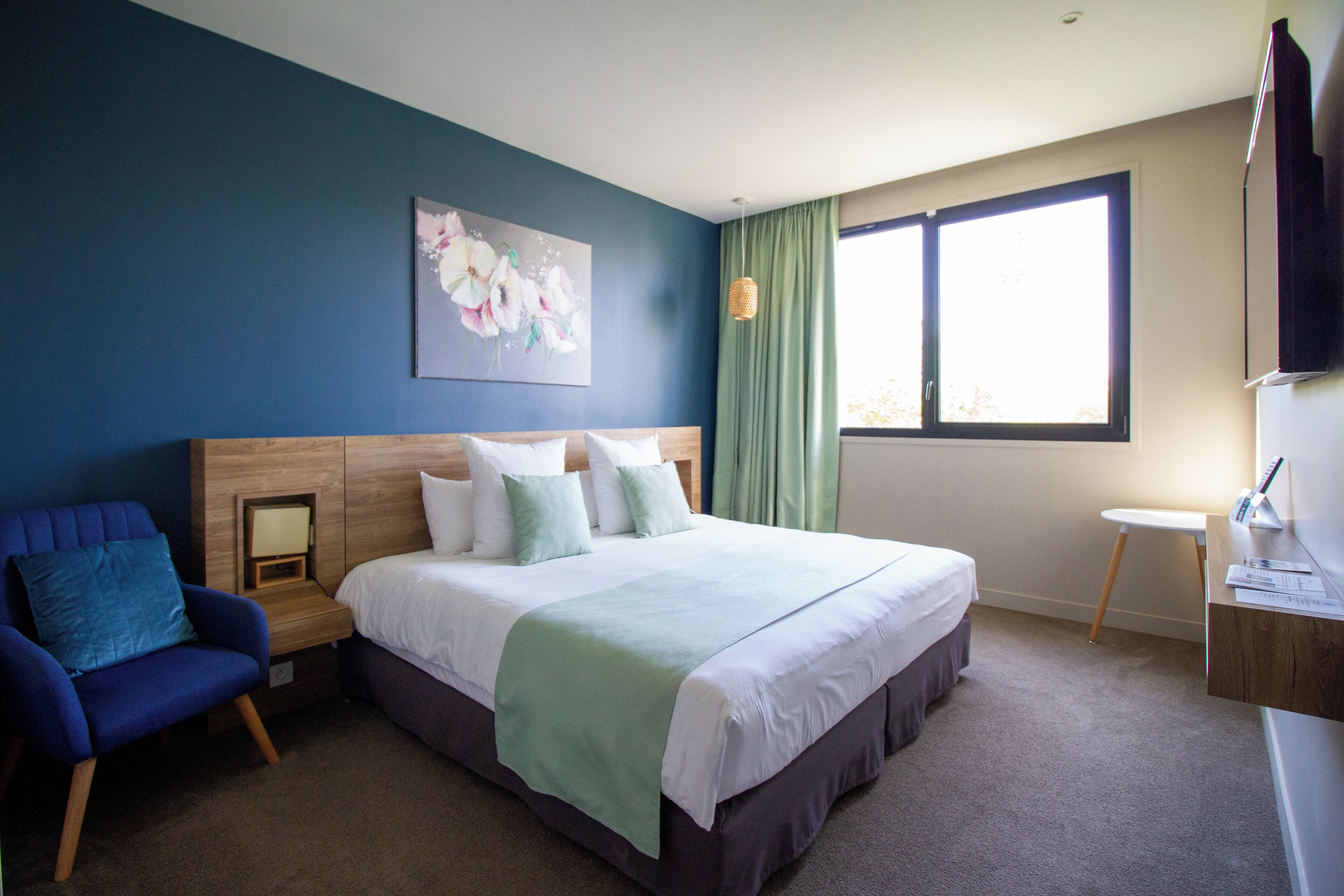 A bedroom with a large bed, a chair, a desk, a window, and a painting on the wall.