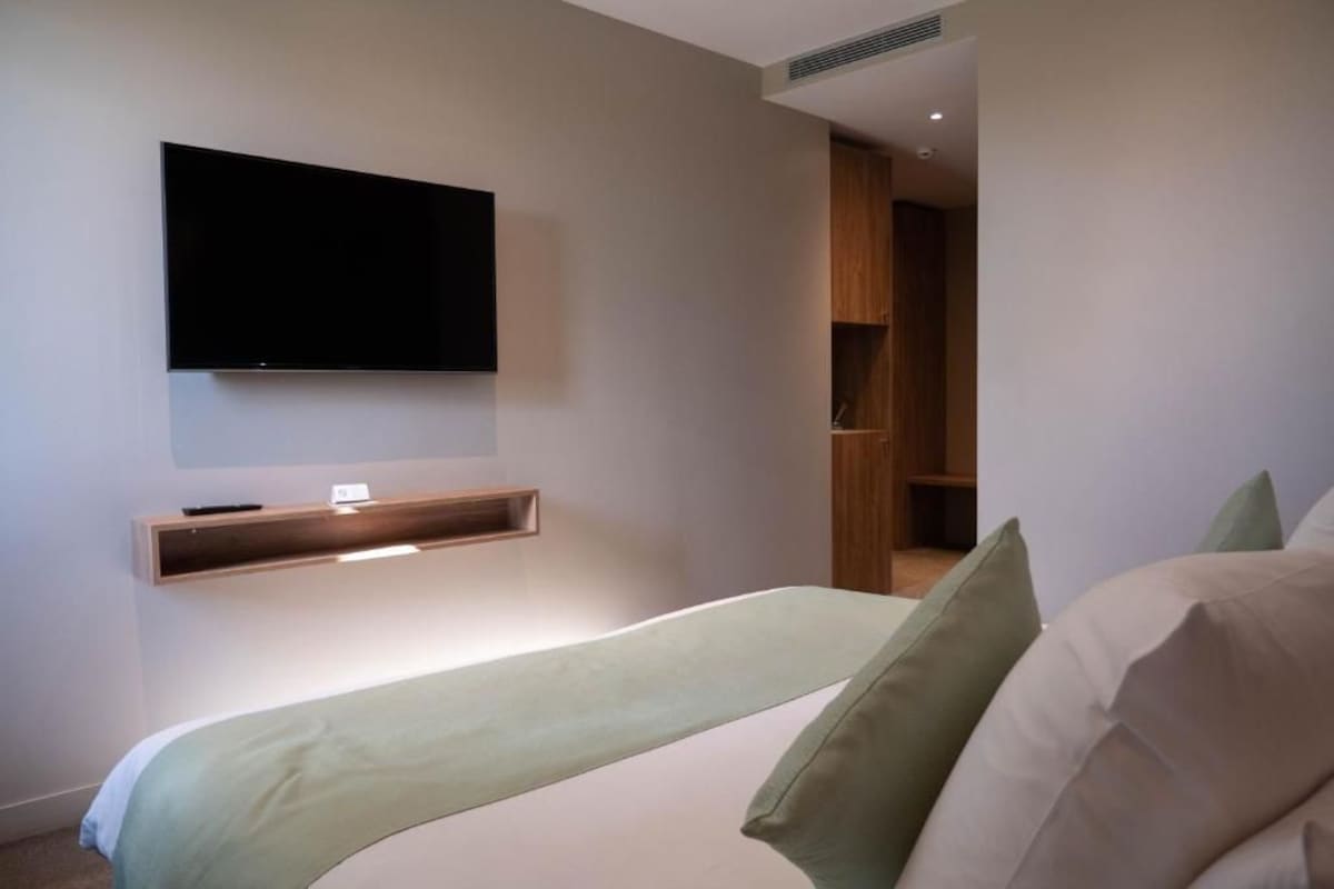 Een moderne slaapkamer met een bed, een wandtelevisie en inbouwplanken.