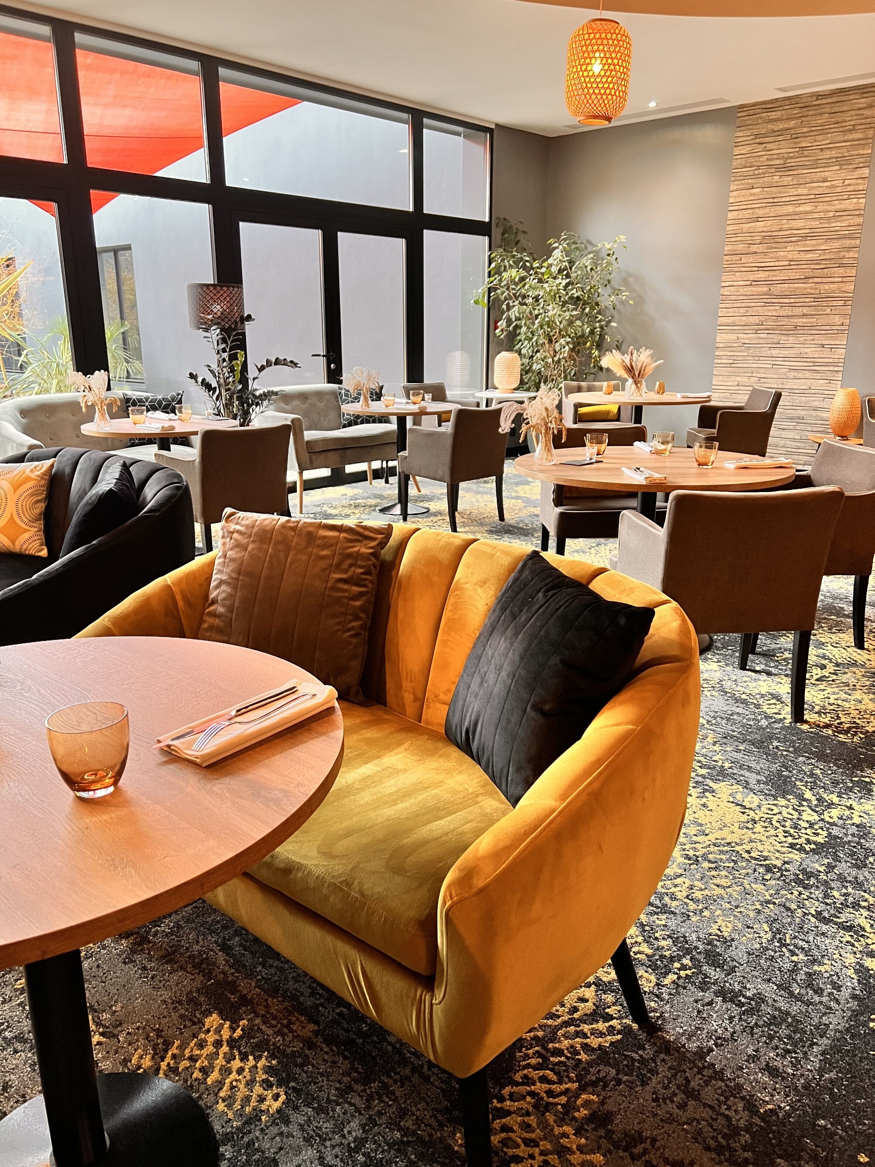 A modern interior with a yellow sofa, round tables, and a large window with an orange awning.