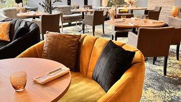 A modern interior with a yellow sofa, round tables, and a large window with an orange awning.