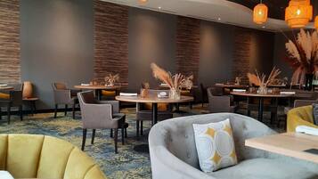 A modern hotel lobby with round tables, sofas, and hanging pendant lights.