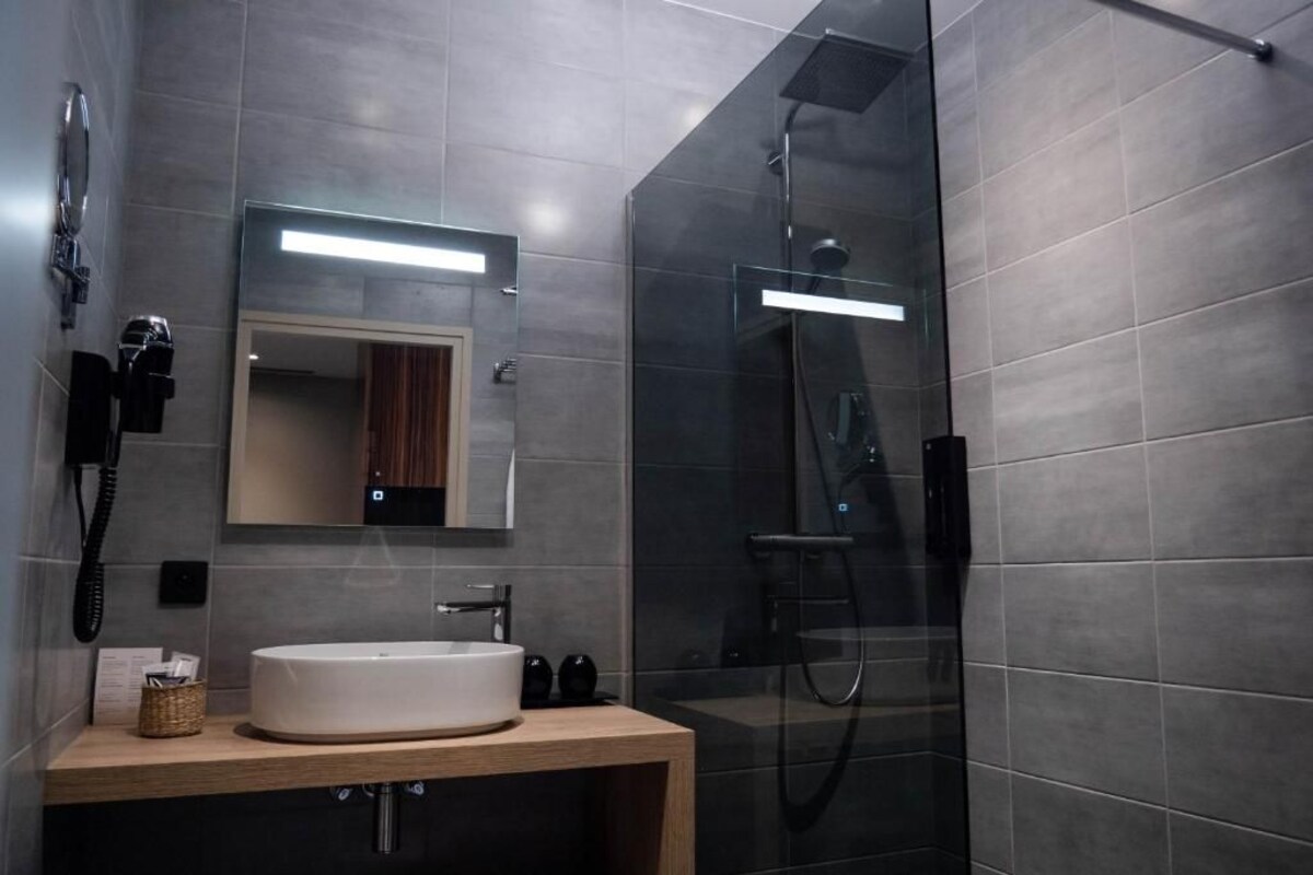 A modern bathroom with a glass-enclosed shower, a large mirror, and a wooden vanity with a white sink.