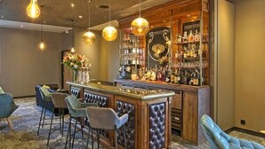 Zona de bar con mostrador de madera, varios taburetes y lámparas colgantes.
