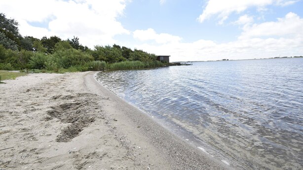 A beach with a wooden structure, clear water, and a distant shoreline. - Apartment in Hippolytushoef for 2 Guest (Hippolytushoef)