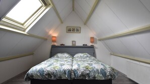 A bedroom with a sloped ceiling, a bed with a floral bedspread, two wall-mounted lamps, a framed picture, and a clock on the wall. - Apartment in Hippolytushoef for 2 Guest (Hippolytushoef)