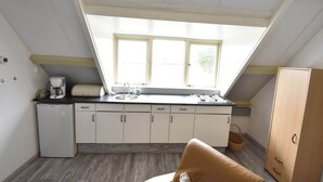 A compact kitchen with a skylight, white cabinets, a small refrigerator, and a wooden cabinet. - Apartment in Hippolytushoef for 2 Guest (Hippolytushoef)
