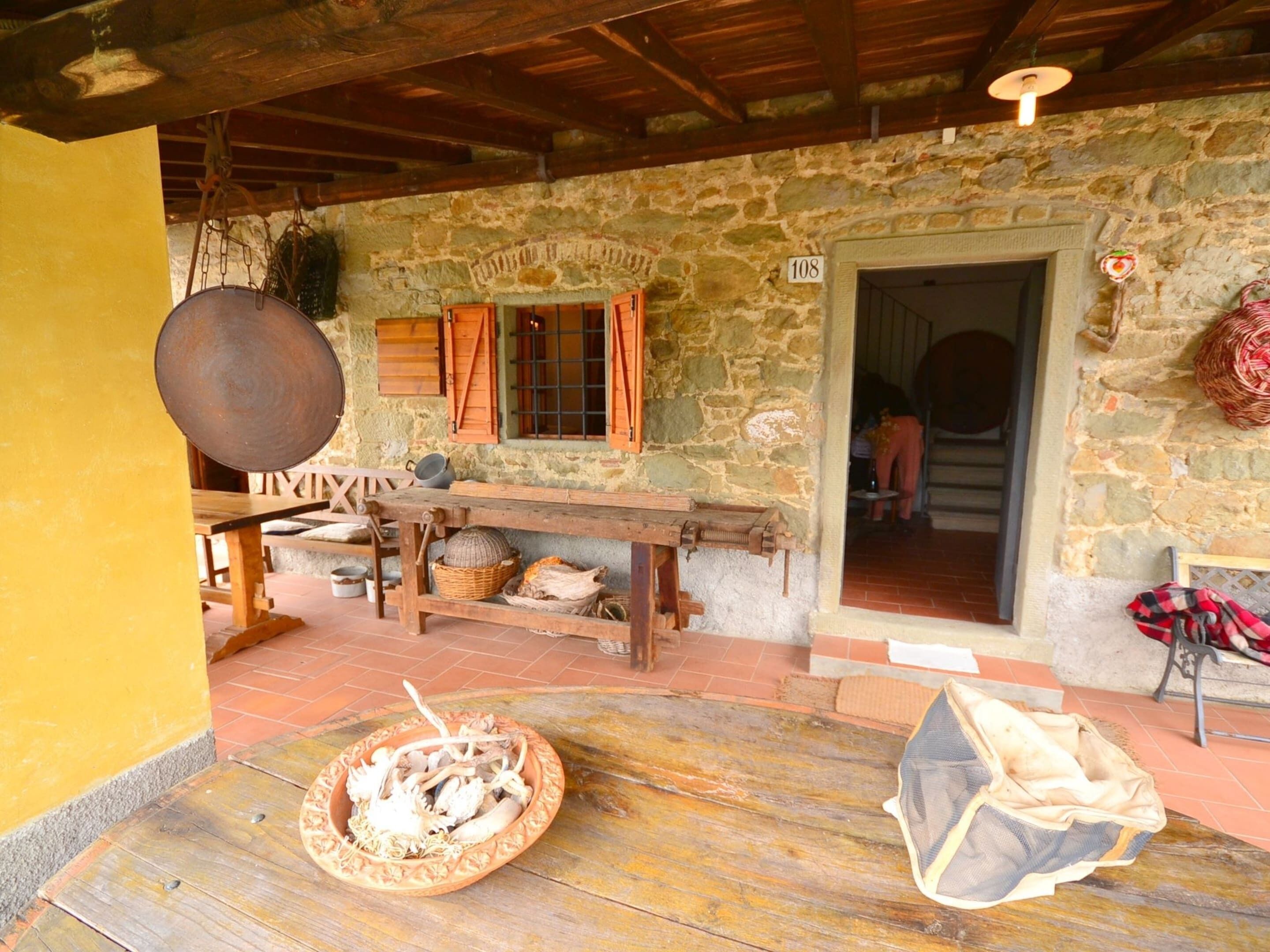 A rustic stone building with a wooden table, a large pot, and a basket of food items.