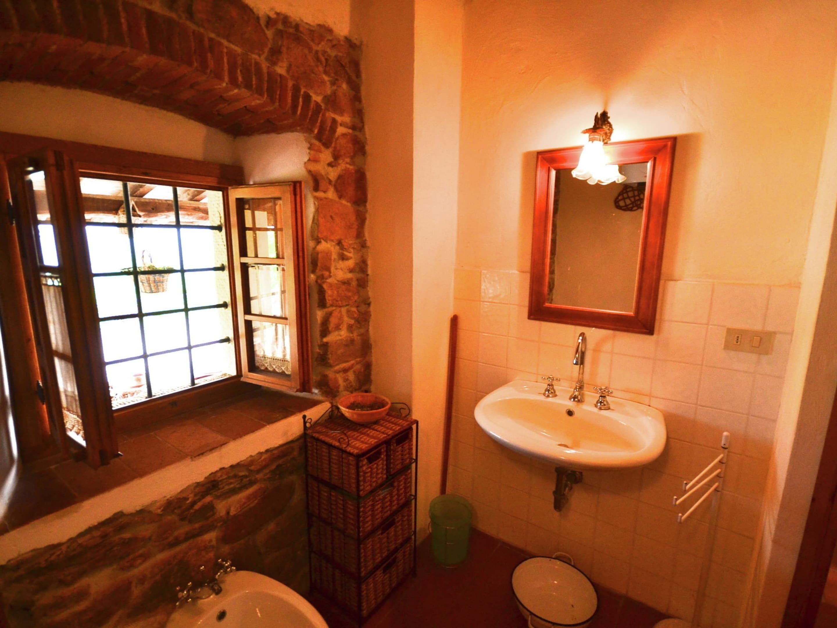 A bathroom with a stone wall, a sink, a mirror, and a window with a view.