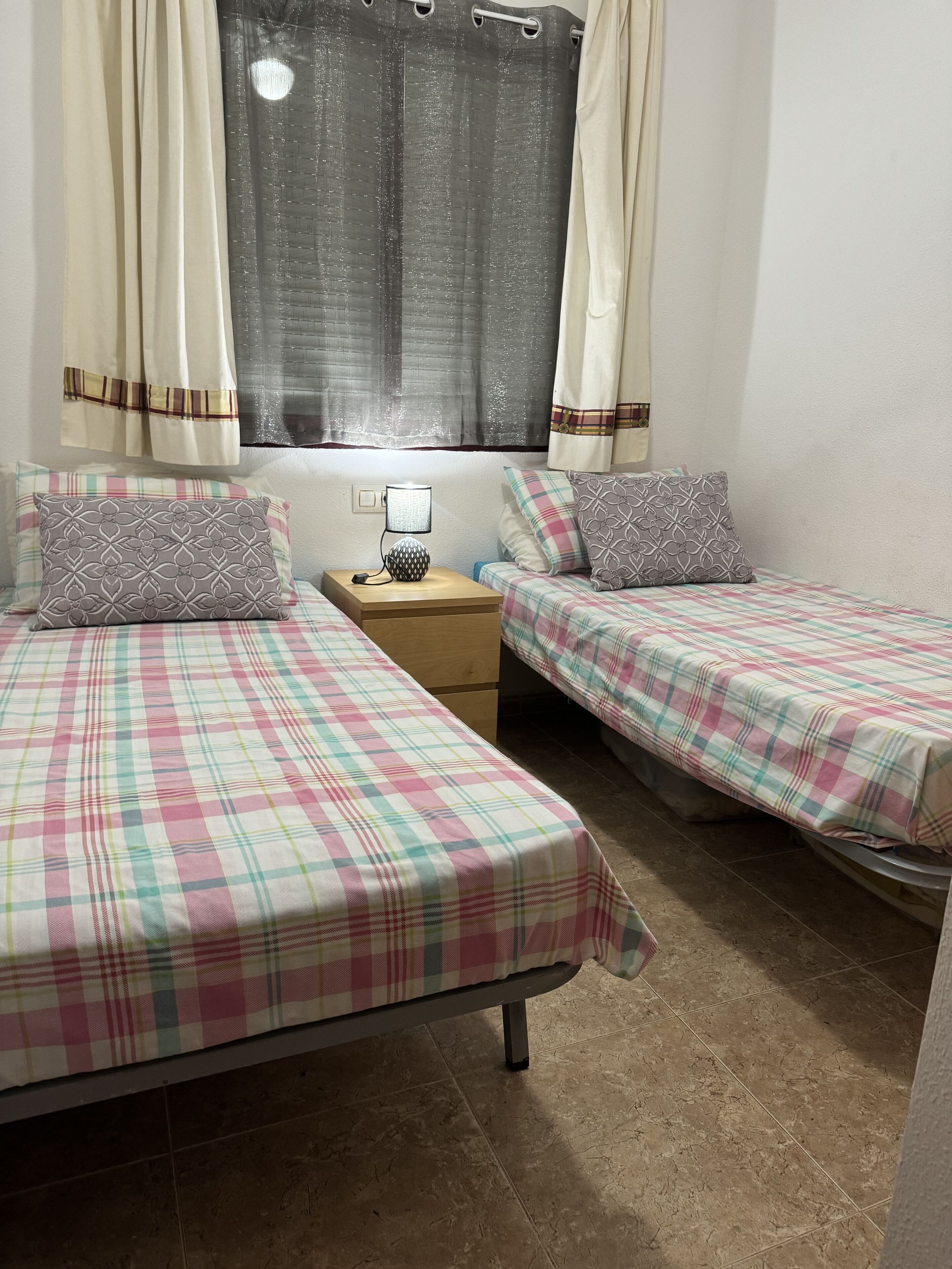 Une chambre avec deux lits, une table de chevet et une fenêtre avec des rideaux.