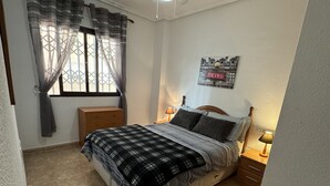 Ein Schlafzimmer mit einem Bett, einem Nachttisch, einer Lampe, einem Fenster mit Vorhängen und einem an der Wand befestigten Schild.