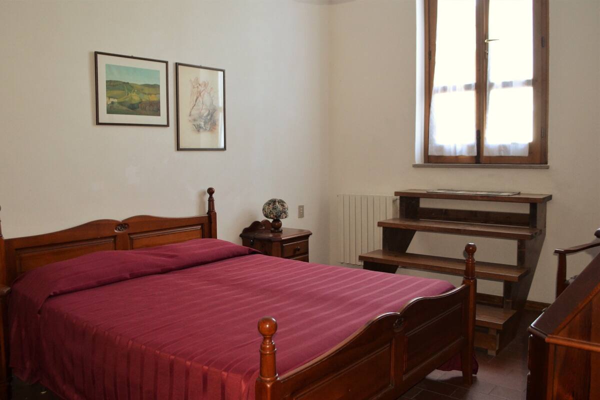 Een slaapkamer met een houten bed, nachtkastje, bureau en raam met gordijnen.