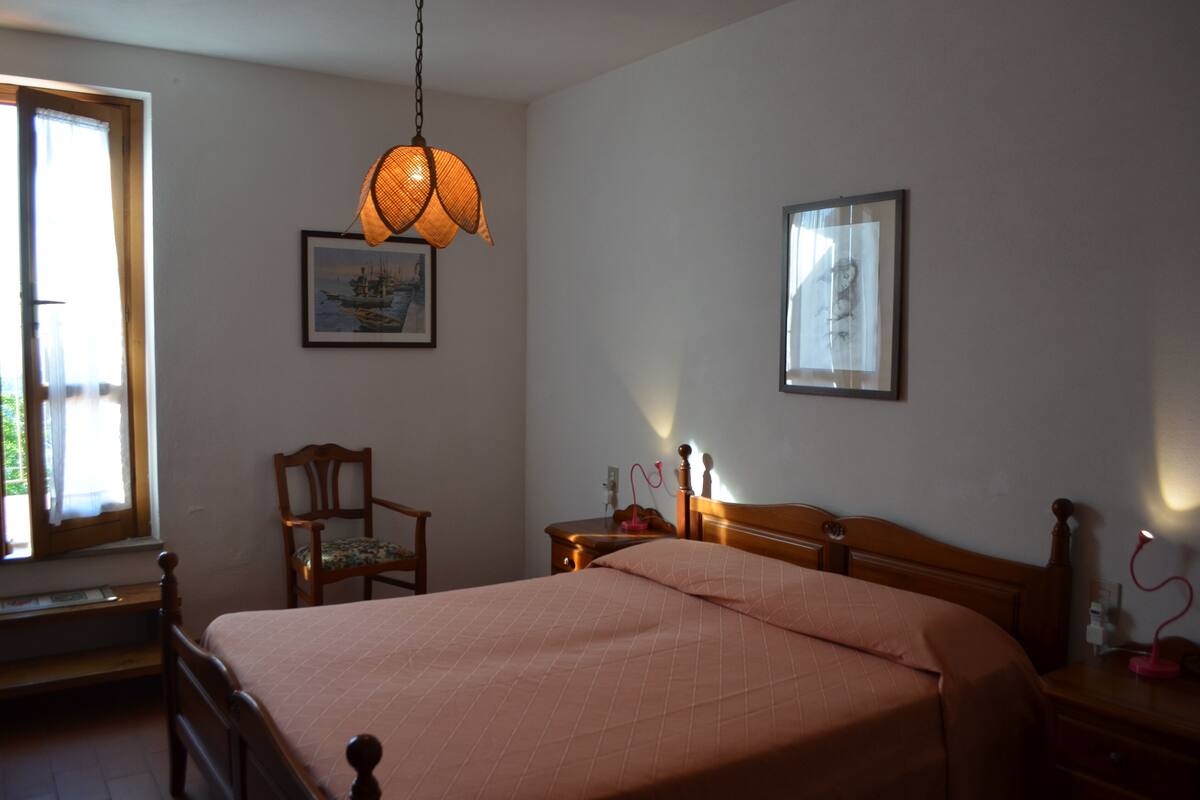 Een slaapkamer met een bed, een stoel, een nachtkastje, een lamp en twee foto's in lijsten aan de muur.
