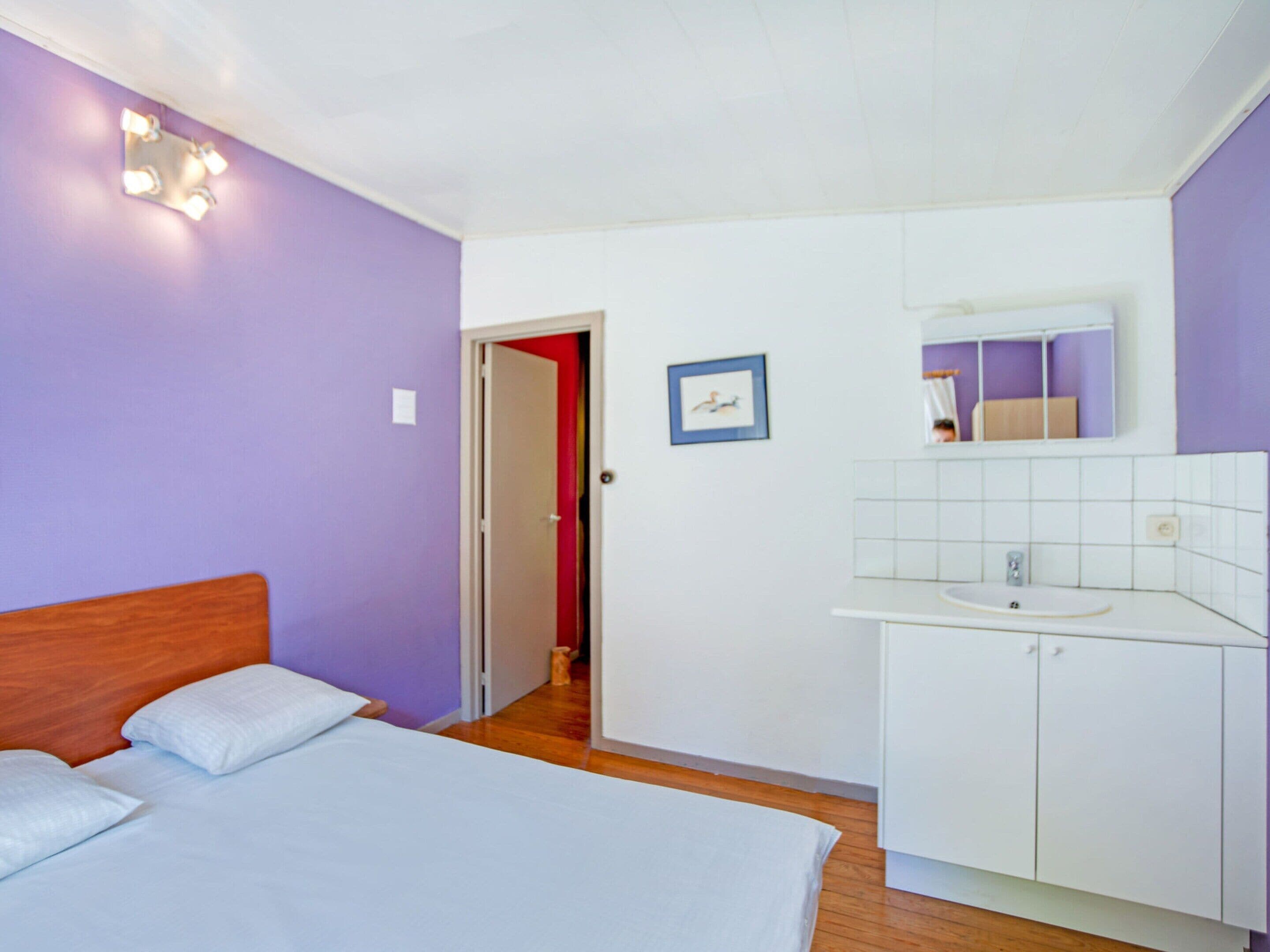 Une chambre à coucher avec un lit, une armoire blanche, un miroir et une porte donnant sur une autre pièce.
