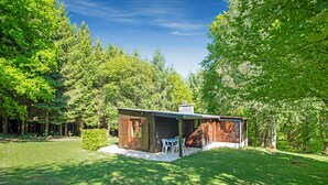 Eine kleine Holzhütte mit Terrasse, umgeben von üppigen, grünen Bäumen.