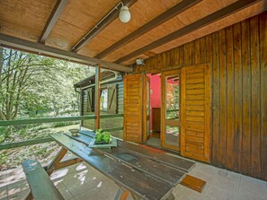 A wooden cabin with a picnic table and a glass door leading to a red room.