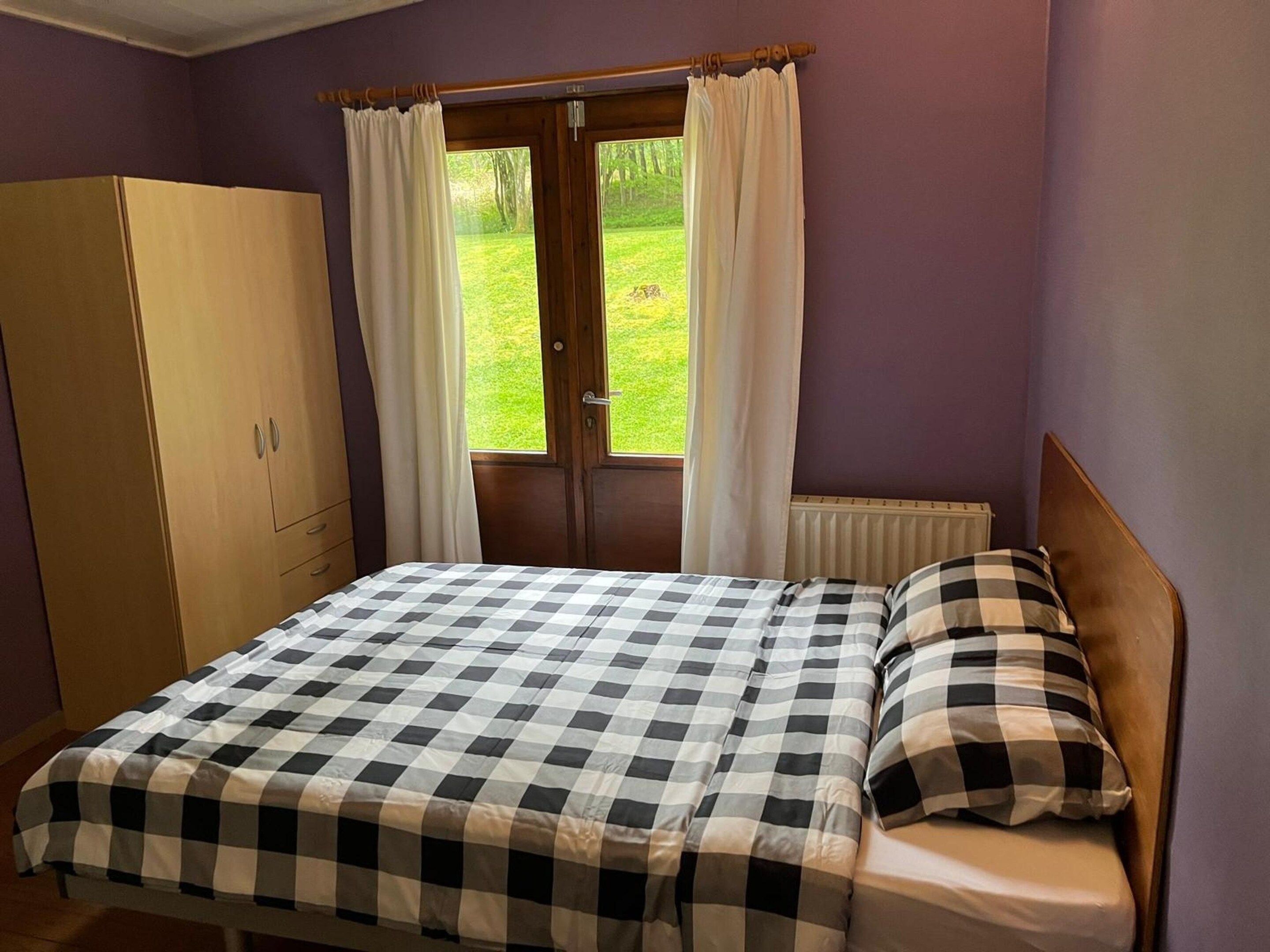 Une chambre à coucher avec un lit, une armoire, une fenêtre avec des rideaux et une vue sur une pelouse verdoyante.