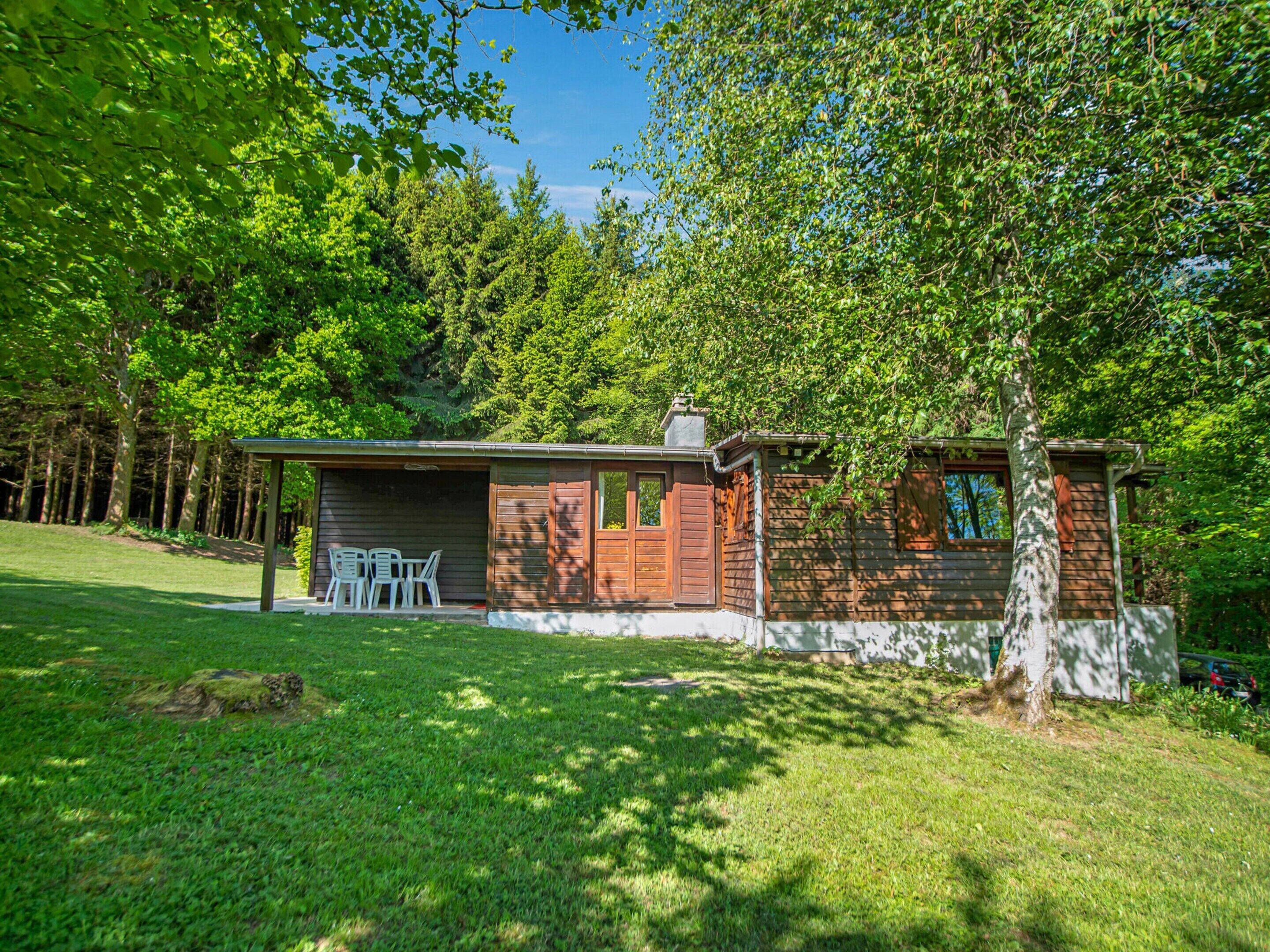 A small cabin with a covered porch and a single window, surrounded by lush green trees.