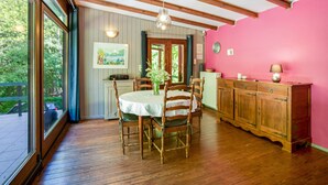 Ein Essbereich mit Holztisch und -stühlen, einer rosa Wand und Blick durch große Fenster.