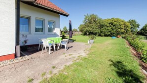 Talo, jossa on patio, jossa on pöytä ja tuoleja, ruukussa oleva kasvi ja nurmikko.