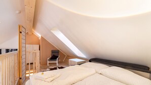 A bedroom with a sloped ceiling, a bed with white bedding, a chair, and a small table. - Apartment in St. Georgen (Bruck an der Grossglocknerstrasse)